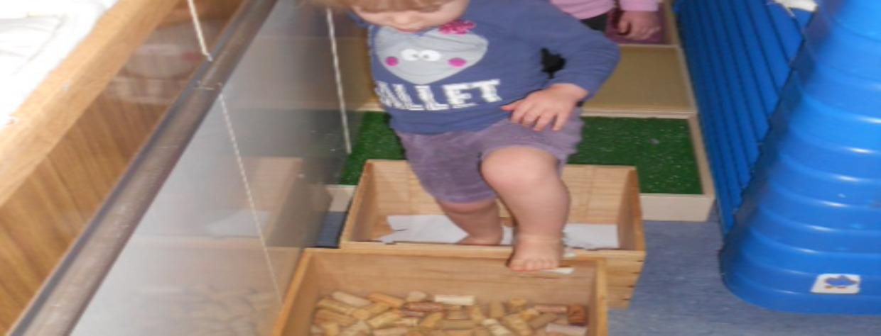 Activité avec un enfant qui marche dans des bacs en bois contenant des textures différentes