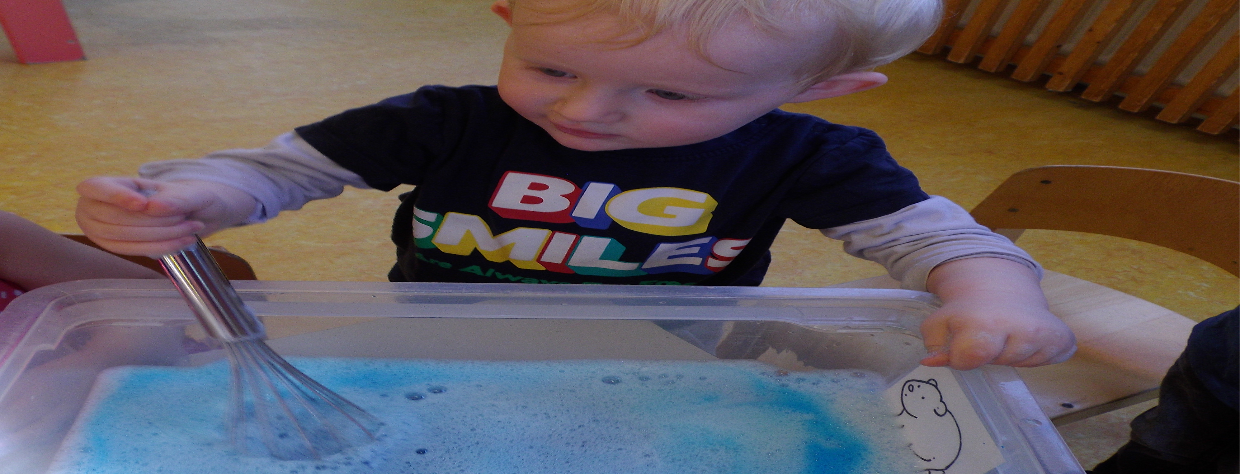 Enfant manipulant un fouet de cusine dans une petite bassine d'eau colorée en bleu