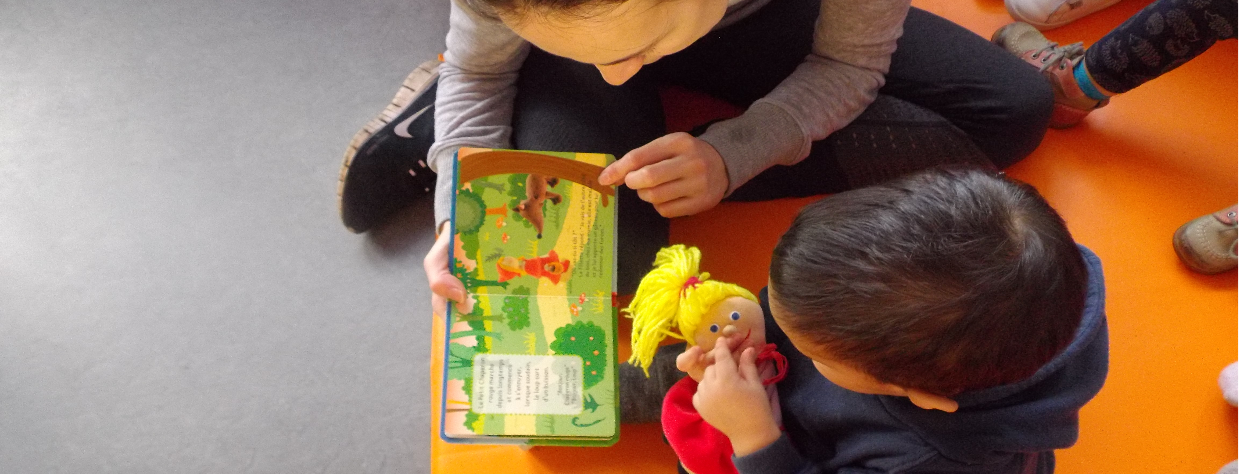 Une puéricultrice lit un livre à  un enfant qui tient une poupée dans ses bras