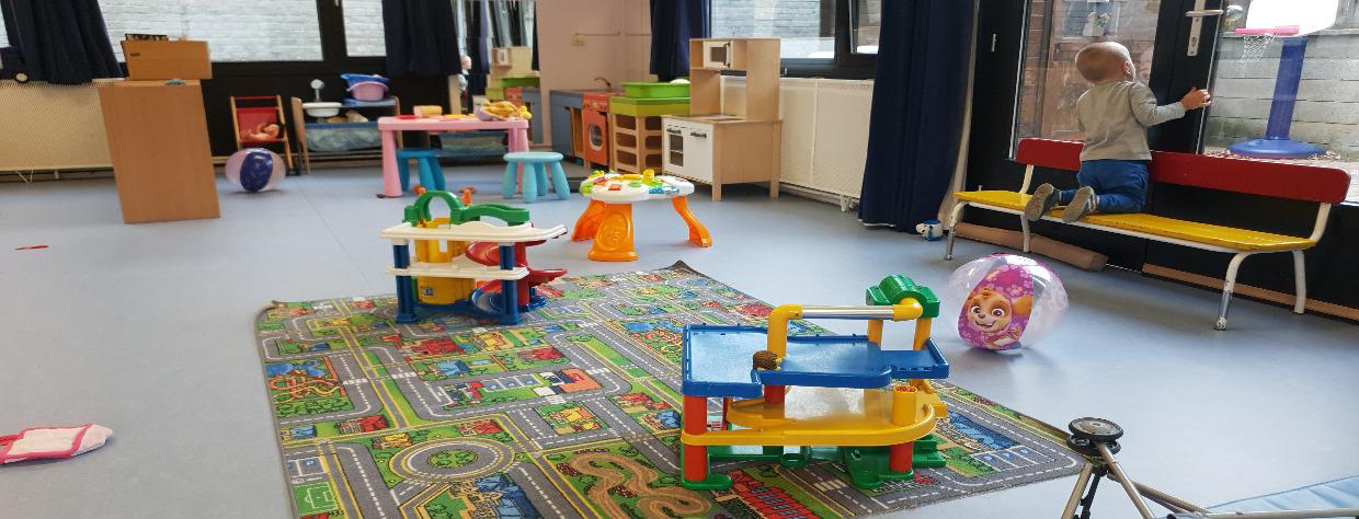Salle d ejeu avec tapis et circuits pour voiture + un enfant sur un banc regardant par la fenêtre